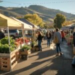 A busy farmers market with people shopping and cars parked in the background The market is bustling with activity and the atmosphere is lively
